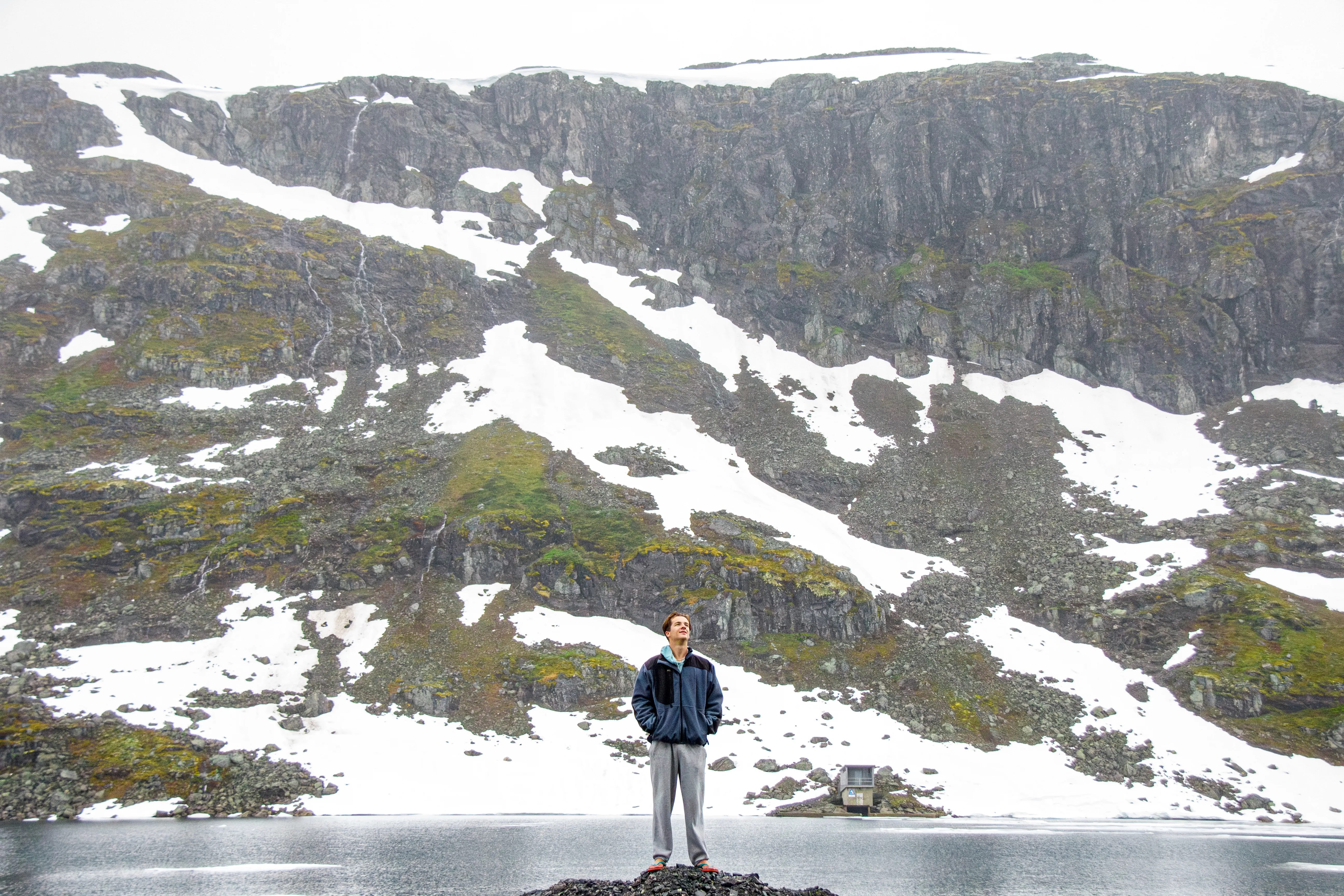 Portrait of a person standing in front of a fjord with mountains in the background.